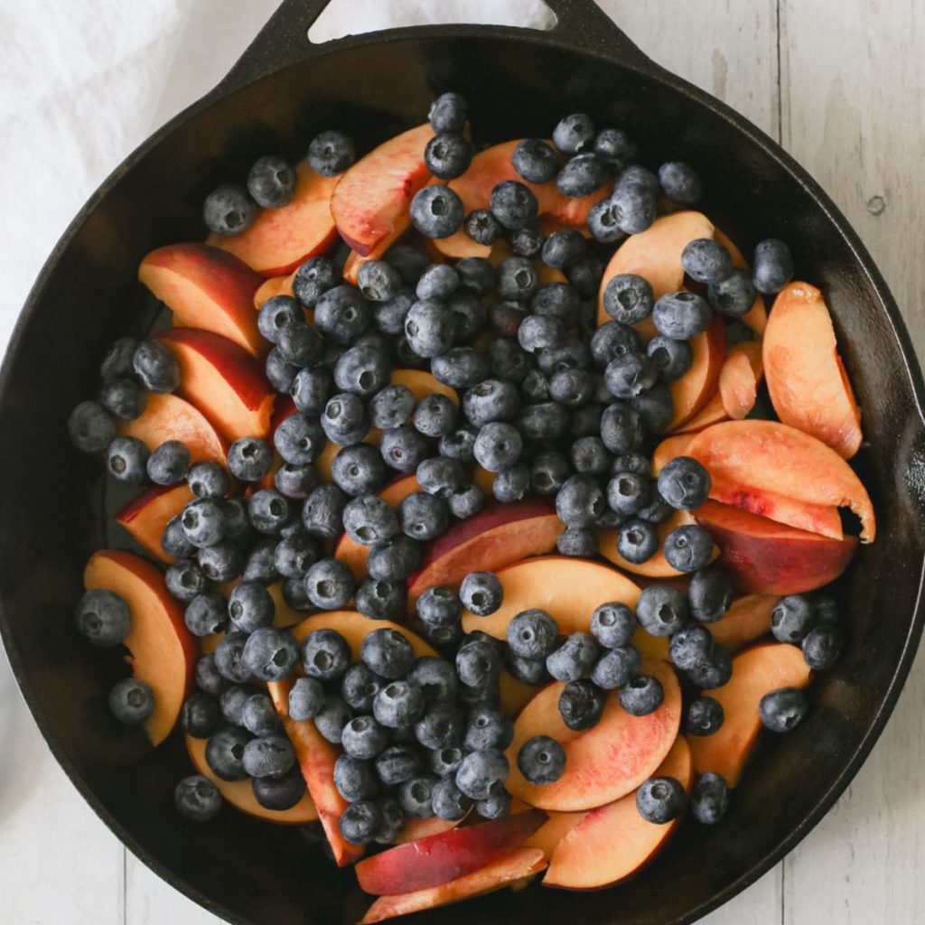 Fresh blueberries and peach slices in a skillet.