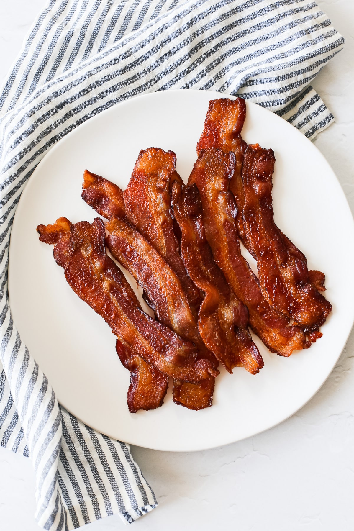 A plate of perfectly cooked bacon fresh warm from the oven without a rack.