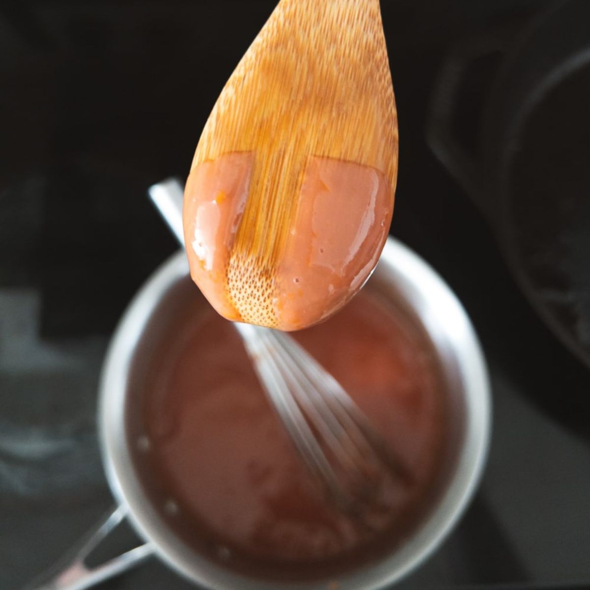 Checking to see if the blood orange curd is done by making a line on the back of a wooden spoon.