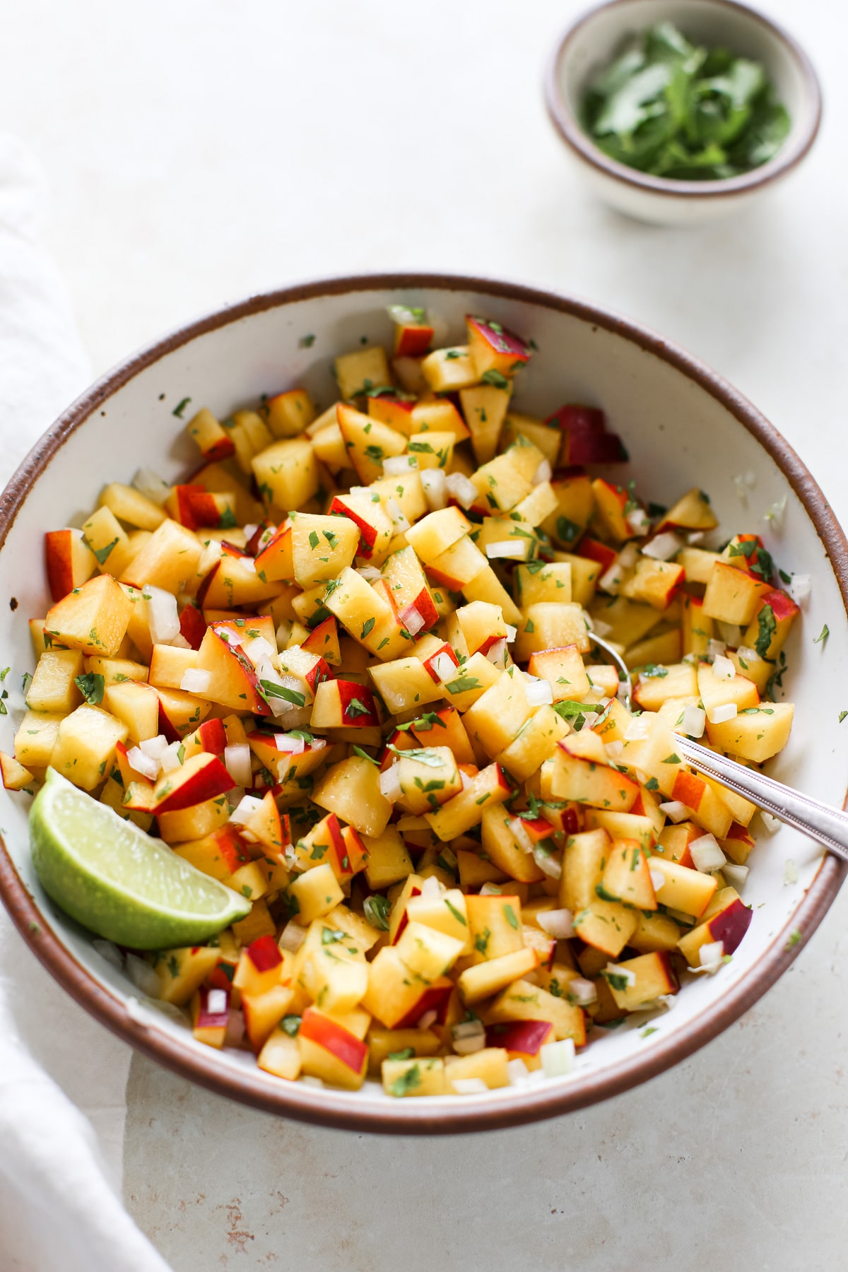 A bowl of nectarine salsa with chopped cilantro and fresh lime wedge.