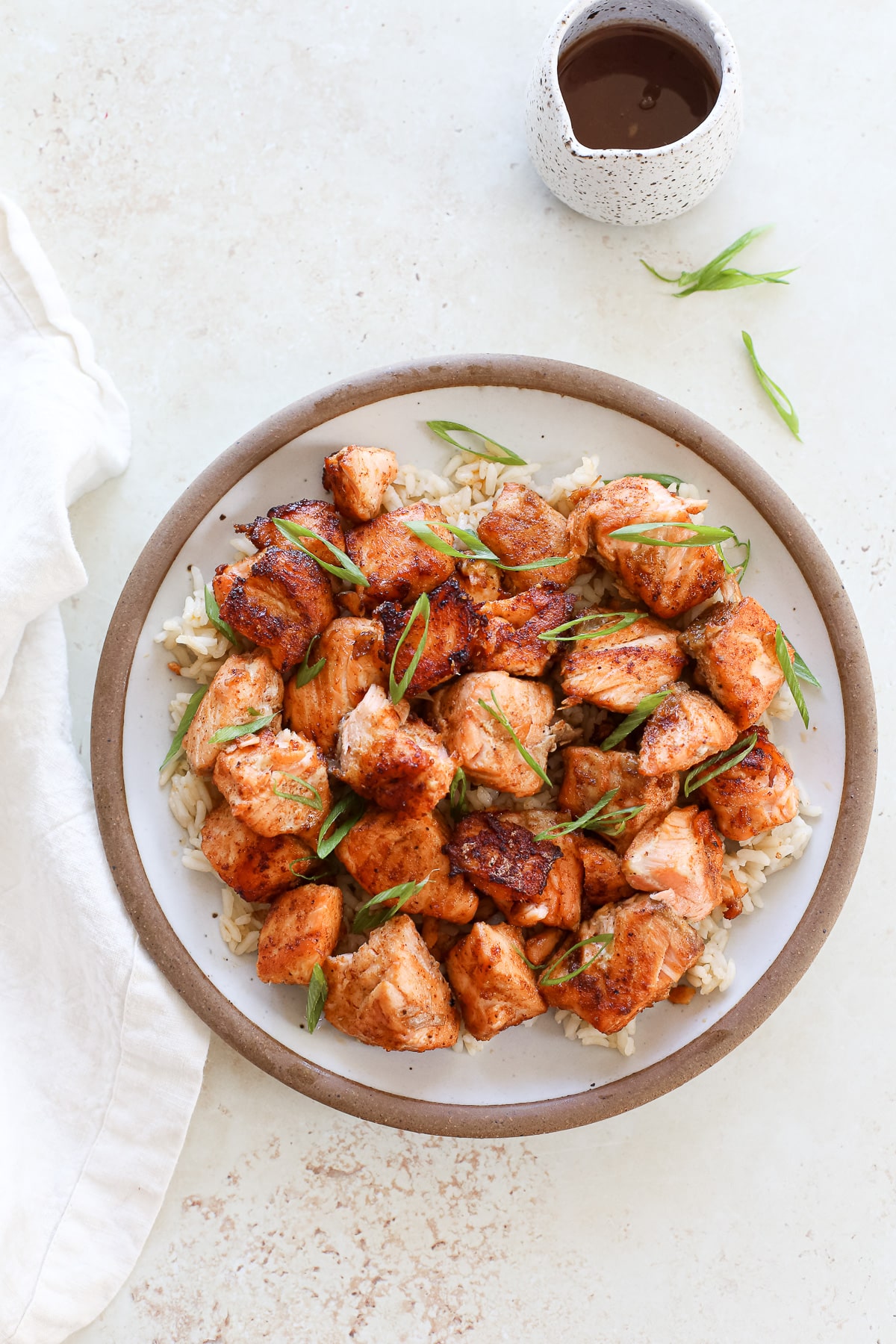 A plate of BBQ salmon bites on a bed of rice and topped with green onions.