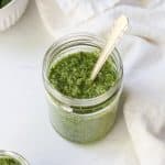 A jar of homemade vibrant green rocket pesto with a spoon.