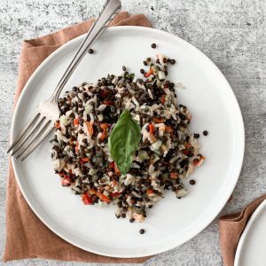 A plate with black beluga lentil salad, bell pepper, rice, and fresh basil.