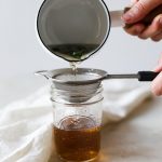 Pouring basil infused simple syrup through a fine mesh strainer.