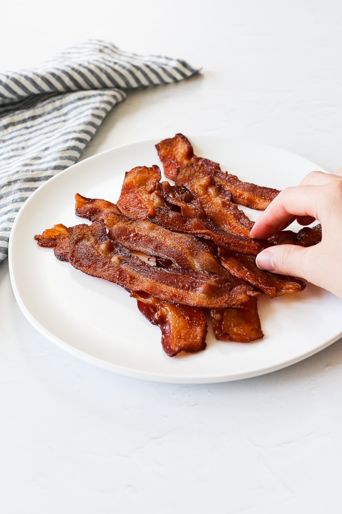 Grabbing cooked warm bacon off a plate that just came out of the oven.