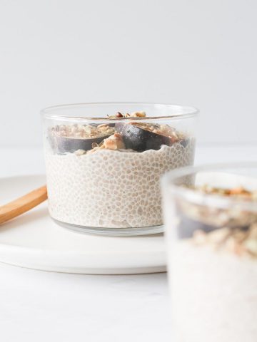 A short glass of overnight chia seed pudding topped with fresh fig slices and dukkah seasoning.