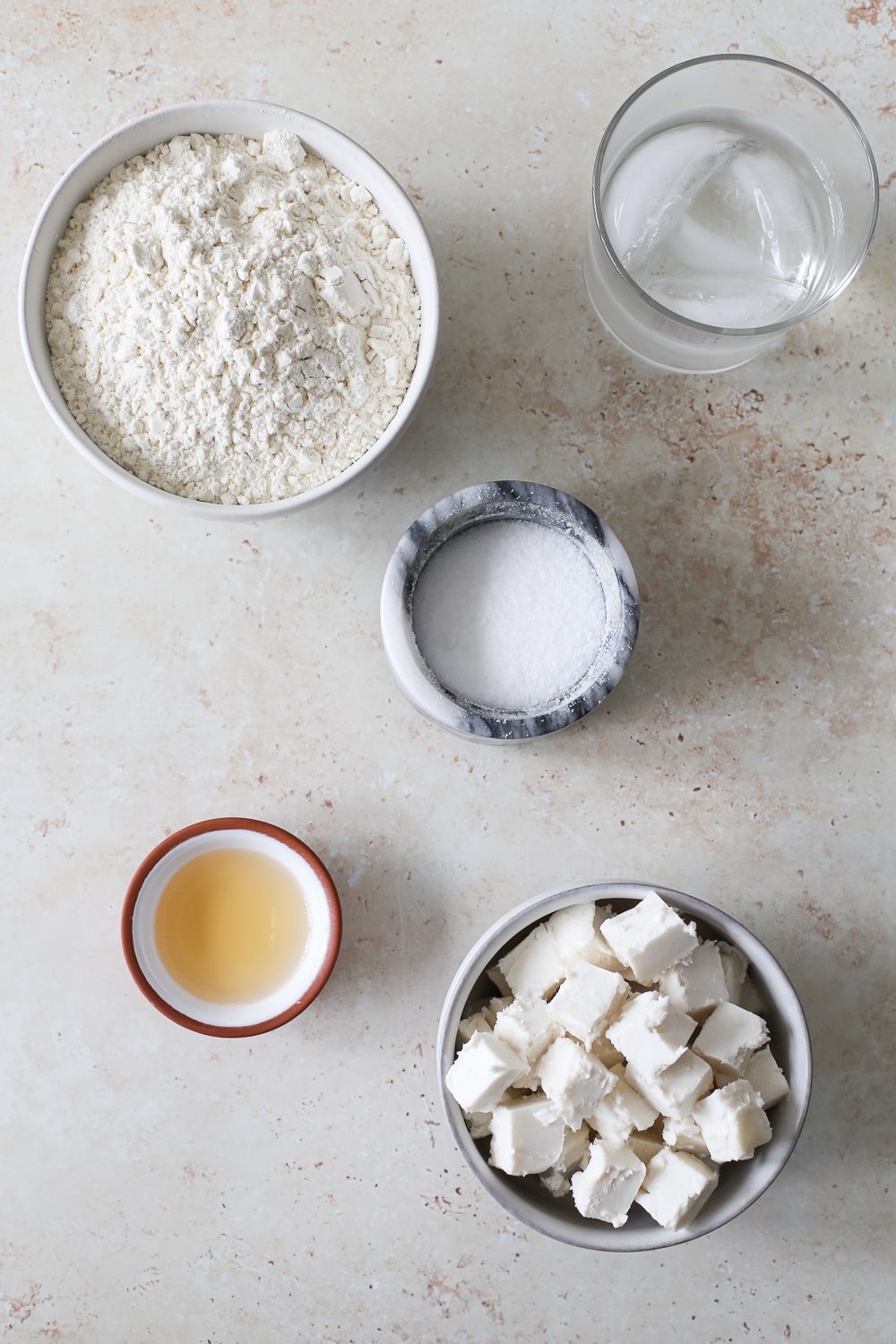 A bowl of flour, cubed cold butter, vinegar, salt, and ice water to make pie crust.