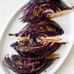 four roasted red cabbage wedges on an oval serving platter
