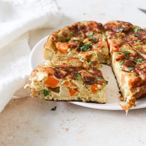 A platter of spanish tortilla with orange sweet potatoes and fresh herbs.