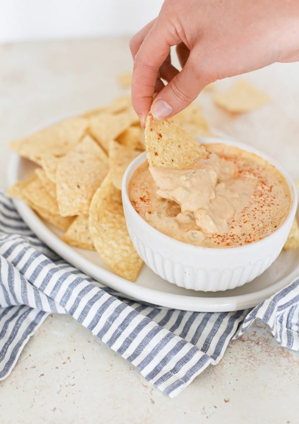 dipping a tortilla chip into a bowl of dairy-free cashew queso