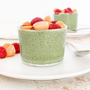Matcha chia pudding on a plate with goldenberries and fresh raspberries.