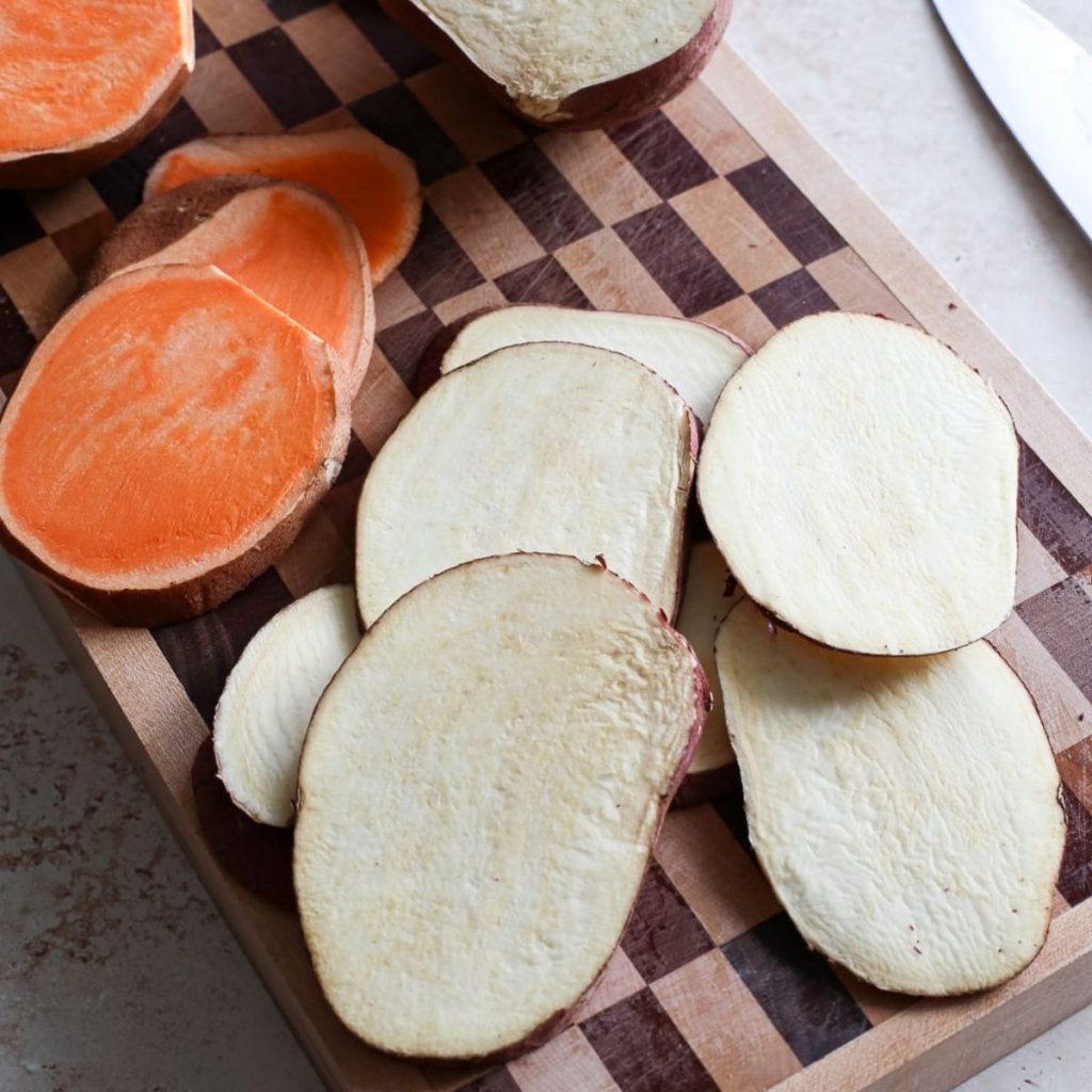 Sliced white and orange sweet potatoes rounds on a cutting board.