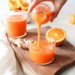 Pouring a glass of fresh orange carrot ginger juice over ice.