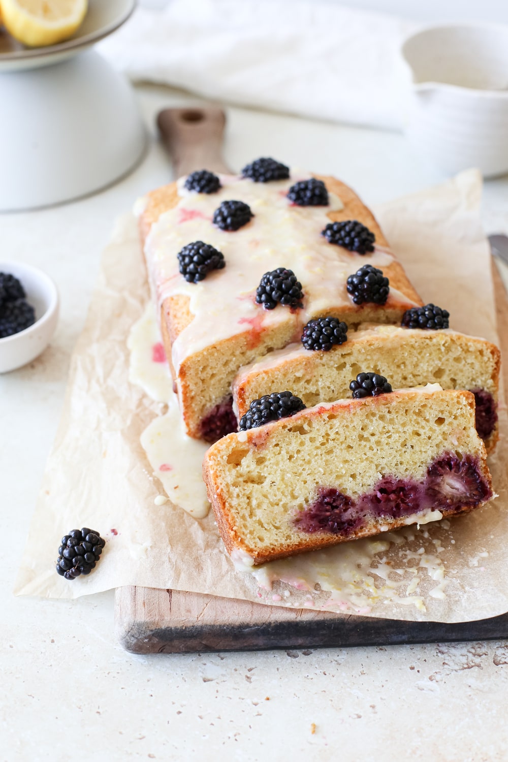 Slices of lemon blackberry bread on a parchment paper lined wooden cutting board.
