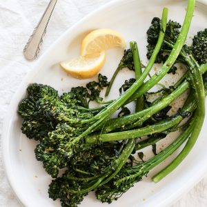 An oval serving platter with broccolini and lemon wedges.