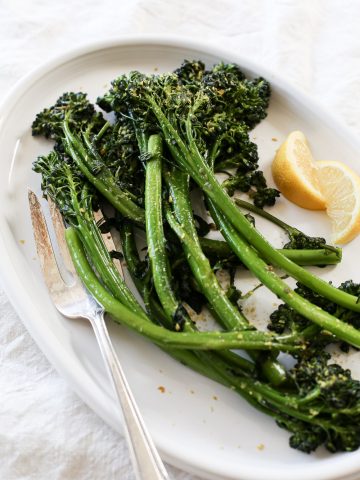 A plate of sautéed broccoletti with garlic and lemon wedges.