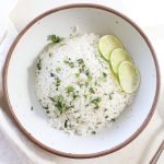 A bowl of homemade coconut lime rice with fresh lime slices and chopped cilantro on top.