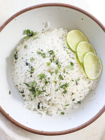 A bowl of homemade coconut lime rice with fresh lime slices and chopped cilantro on top.