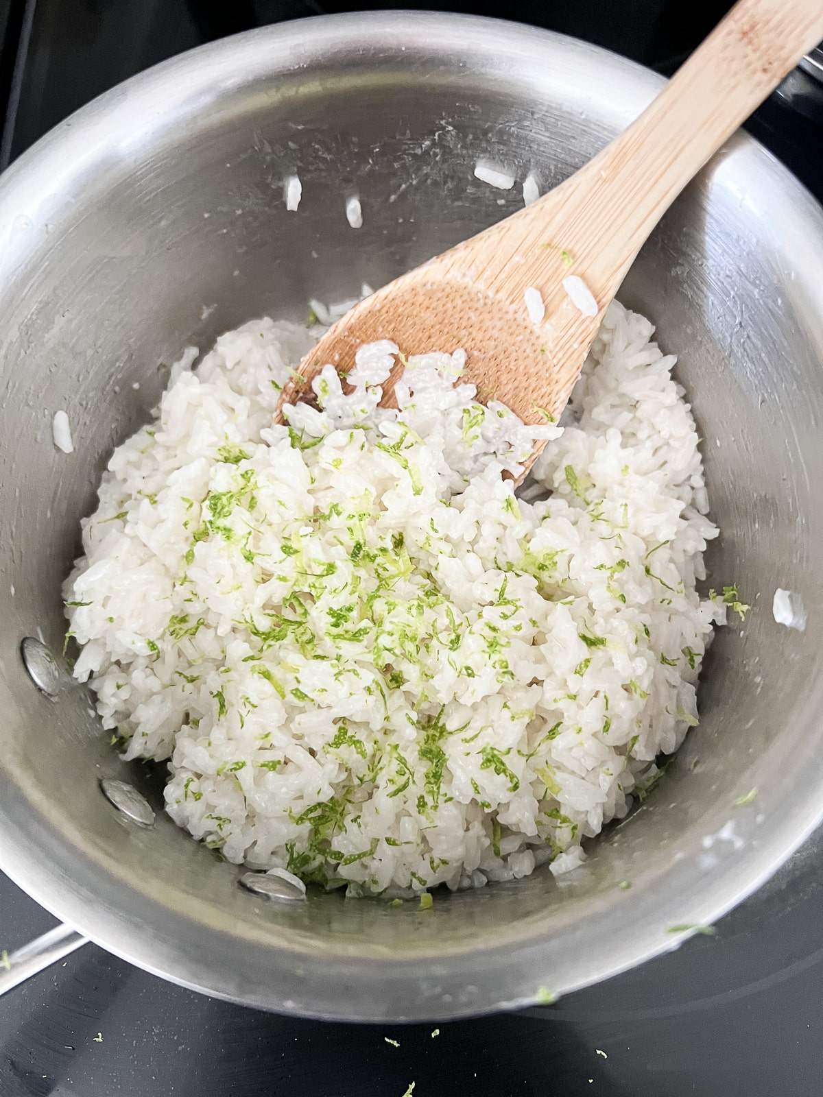 Rice in a saucepan with lime zest and a wooden spoon.