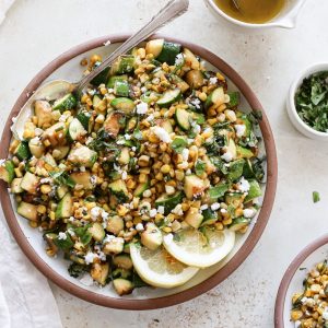 A large serving platter with zucchini corn salad and feta crumbles.