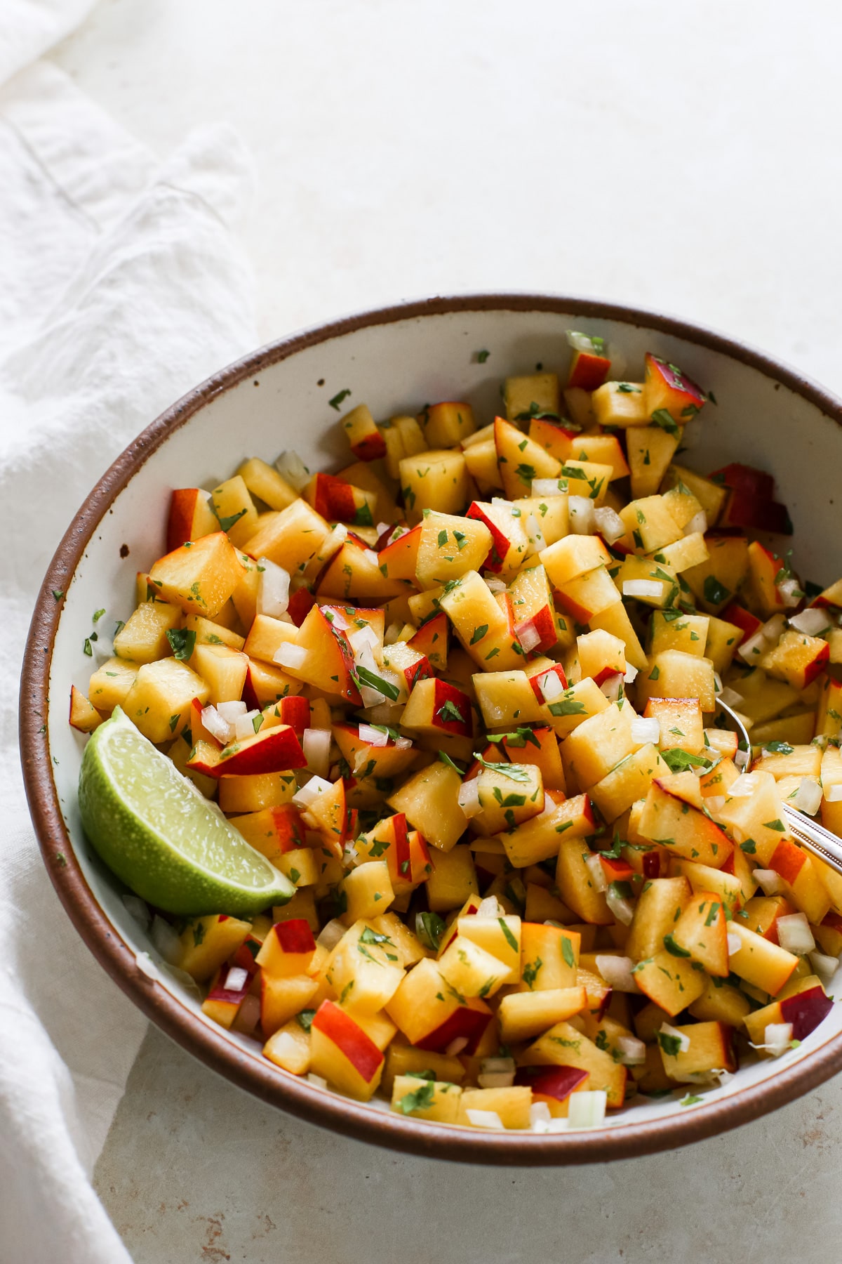 A bowl of fresh nectarine salsa with cilantro and a lime wedge.