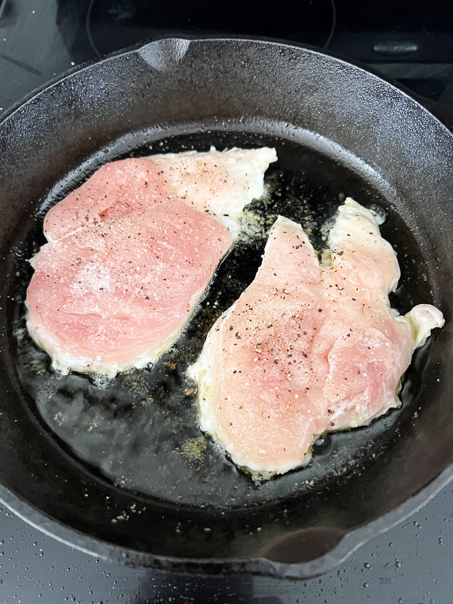 Searing seasoned chicken breasts in an oiled skillet.