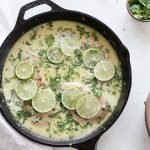 A large skillet with Thai coconut lime chicken served next to a bowl of fresh cilantro.