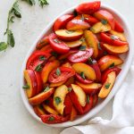 Peach and tomato wedges on an oval platter with torn fresh mint leaves.