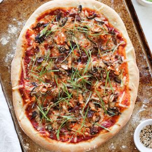 A large Korean pizza with gochujang tomato sauce, green onions, bacon, and mushrooms.