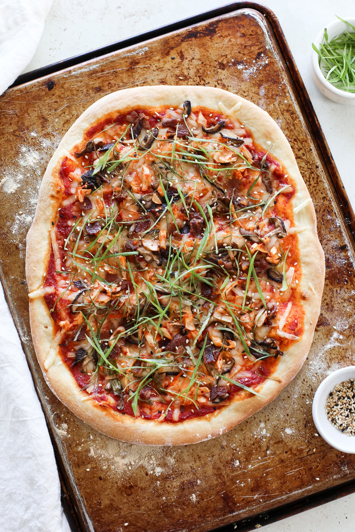 A large pizza with kimchi, bacon, green onion, mushrooms, and a gochujang sauce.