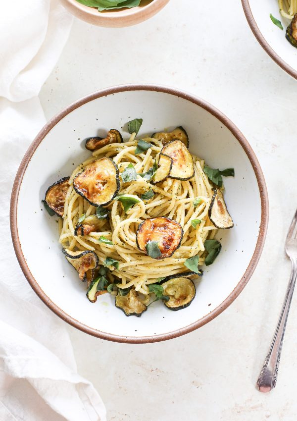 A bowl of spaghetti with fried zucchini rounds in a zucchini sauce with fresh torn basil leaves.