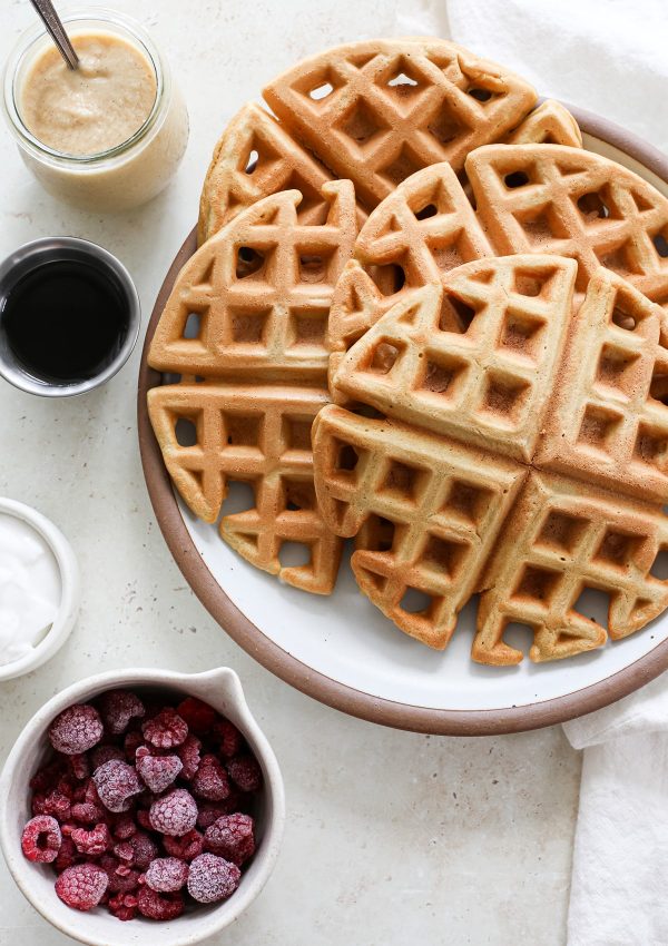A plate of large round oat flour waffles next to bowls of toppings.