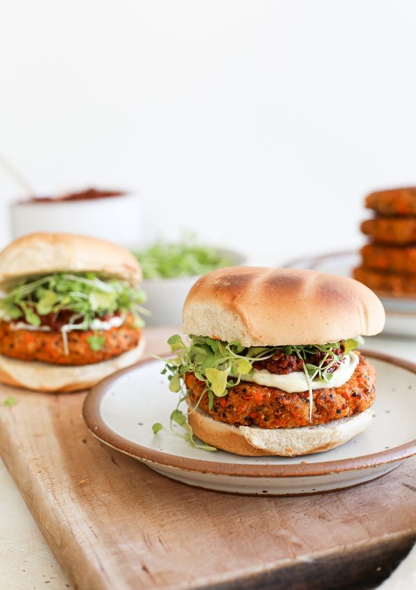A quinoa veggie burger on a grilled bun with greens and sauce.
