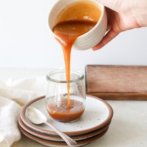 Pouring a thick, amber-colored miso caramel into a jar.
