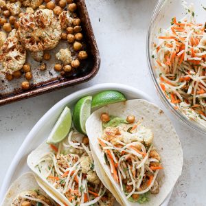 Roasted chickpea and cauliflower tacos on a plate with fresh lime wedges and a carrot jicama cilantro slaw.