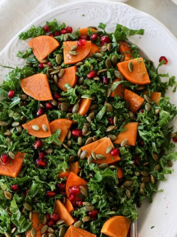 A large platter of persimmon salad with kale, pomegranate seeds, and toasted pumpkin seeds.