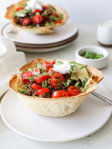 Two taco salad bowls with ground beef, black beans, cilantro, tomatoes, and avocado.