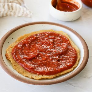 Tomato paste pizza sauce spread onto a small pizza crust.