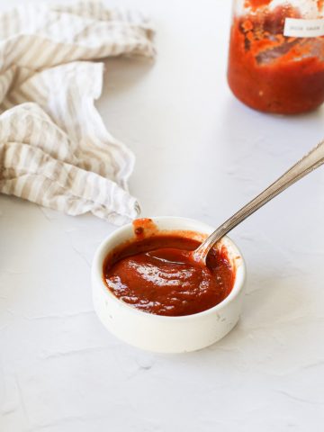 A small bowl of tomato paste pizza sauce with a spoon.