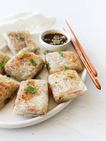 Crispy rice paper dumplings on a serving platter with dipping sauce and chopsticks.
