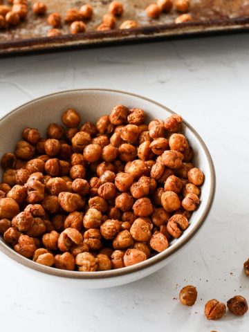 A bowl of crispy baked garbanzo beans/chickpeas with a few on the counter next to the bowl next to a baking sheet.