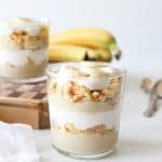 Two glasses with layers of dairy-free banana pudding, crushed vanilla wafers, dairy-free coconut whipped cream, and fresh banana slices.