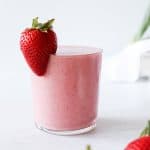 A glass of strawberry banana smoothie with a whole fresh strawberry on the rim.
