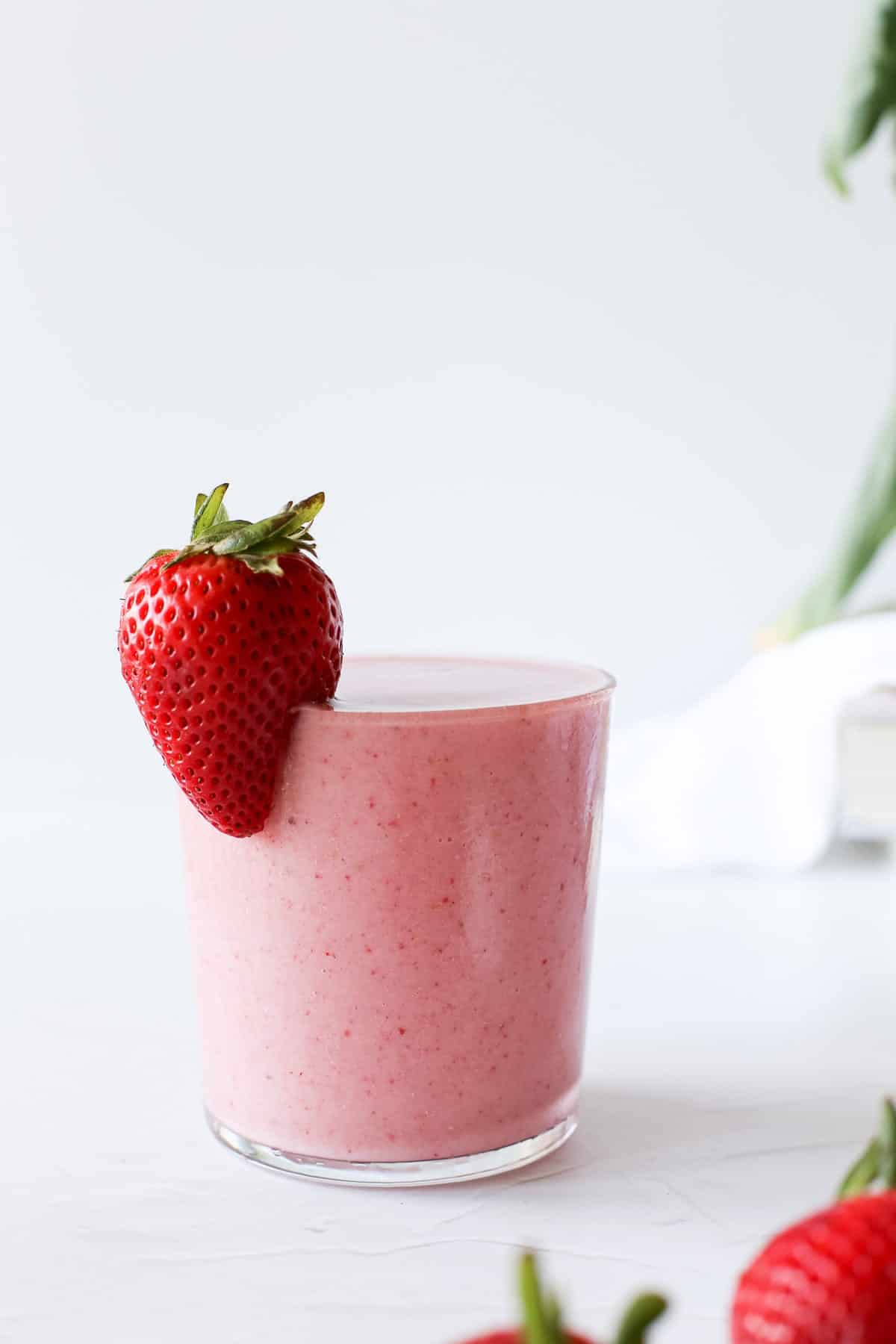 A glass of strawberry banana smoothie with a whole fresh strawberry on the rim.