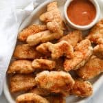 A platter of crispy fried chicken bites without buttermilk with a small jar of red dipping sauce.