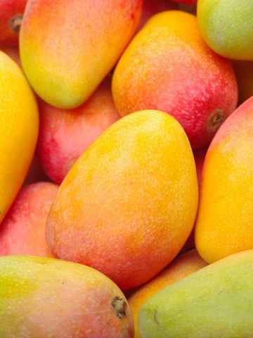 A pile of fresh mangoes with red, yellow, orange, and green skin.