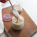 A spoonful of thick homemade dairy free sweetened condensed milk dripping off a spoon into a jar.