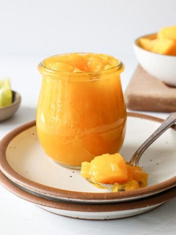 A spoonful of mango compote next to a jar.