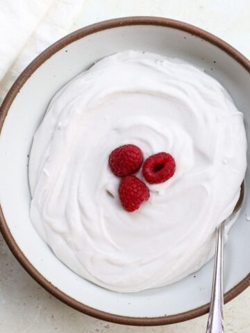 A bowl of homemade dairy free whipped cream with raspberries and a spoon.