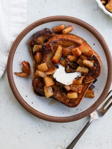 A plate with a stack of dairy free french toast with a pat of vegan butter and sauteed cinnamon diced apples.